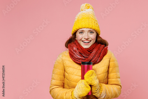 Smiling fascinating charming happy young woman 20s years old wears yellow jacket hat mittens looking camera hold thermal cup coffee tea isolated on plain pastel light pink background studio portrait.