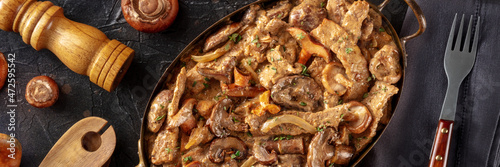 Mushroom beef stroganoff panorama. Meat with champignons, boletus and ceps in a creamy sauce, in a skillet, shot from the top on a black background
