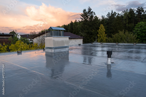 Flat roof covered with bitumen membrane and silver lacquer with chimney on a private house. Reflections after rain