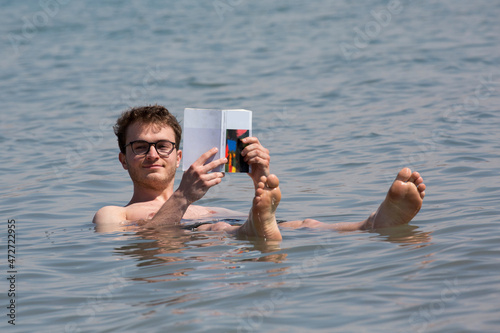 Junger, attraktiver Mann liest Buch im Toten Meer (Israel/Jordanien)