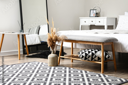 Vase with dry reed and bench near bed in stylish bedroom