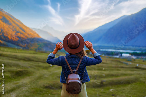 Back view of hipster girl wanderer wearing hat and backpack traveling alone on mountain valley in Georgia country