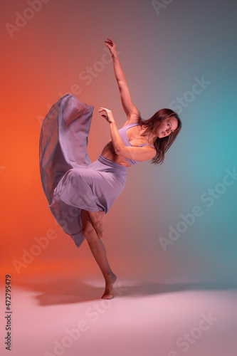 Portrait of young flexible contemp dancer dancing isolated on gradient blue orange background in neon.