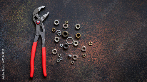 Top view of adjustable universal pliers for repair and assorted nuts on dark rusty background with copy space