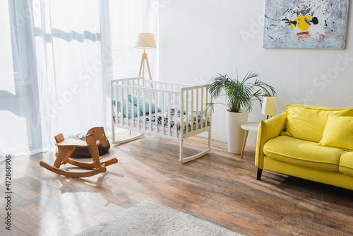 spacious room with yellow sofa, baby crib and rocking horse.