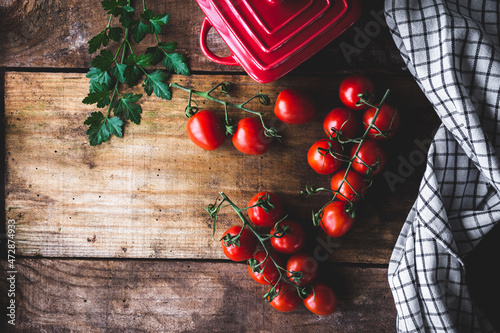 vista superior de ramas de tomates cherry sobre una mesa de madera rústica, con perejil, una mini cocotte y un trapo de cocina, con espacio en blanco