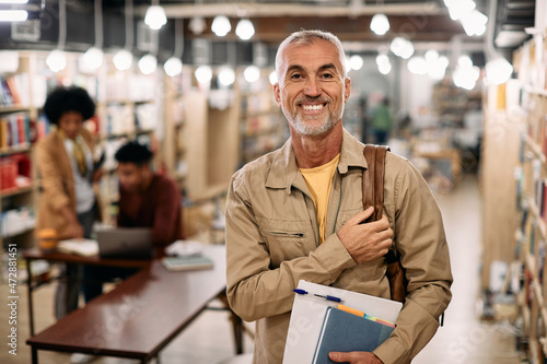 Happy mature student stands at university library and looks at camera.