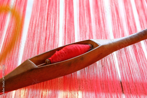 close up red yarn in wood shuttle on red yarns in local loom weaving.