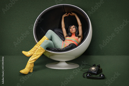 Young woman from the 60s sitting in a vintage ball chair, her rotary dial telephone off the hook at her feet