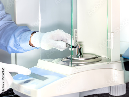 A operator's hand is holding steel calibration weight to place on the analytical balance. Concept of quality control in a laboratory.