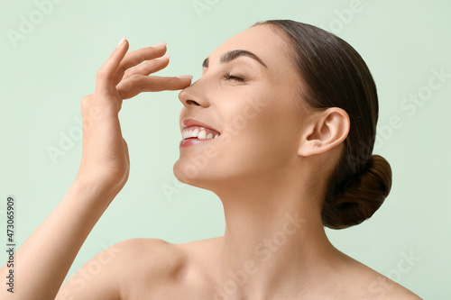 Young woman with healthy skin touching nose on color background