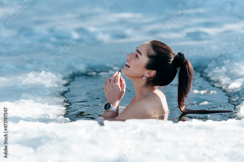 Girl with bikini and a watch in frozen lake ice hole. Woman hardening the body in cold water. Good immunity is protection against many diseases. Vintage color filter