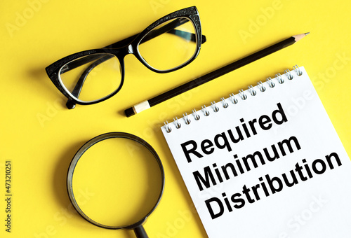 Required minimum distributions RMD phrase written on a notebook with glasses, magnifying glass and pencil