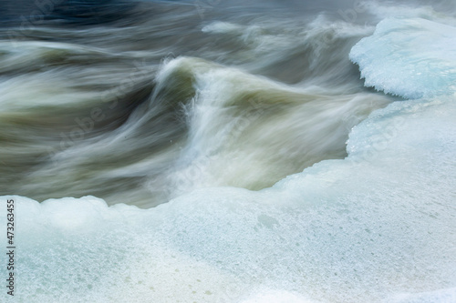 Long exposure shot of fast flowing wintry river with ice banks