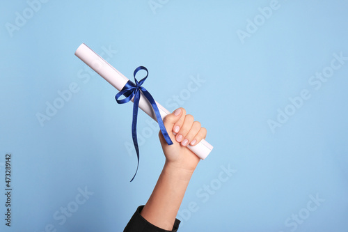 Student holding rolled diploma with ribbon on light blue background, closeup