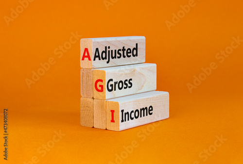 AGI adjusted gross income symbol. Concept words AGI adjusted gross income on wooden blocks. Beautiful orange table, orange background, copy space. Business and AGI adjusted gross income concept.