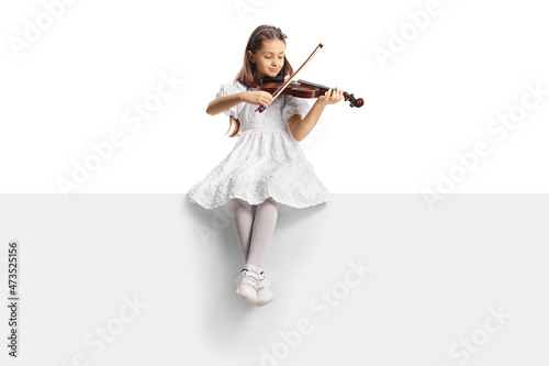 Full length portrait of a girl in a white dress sitting on a blank panel and playing a violin