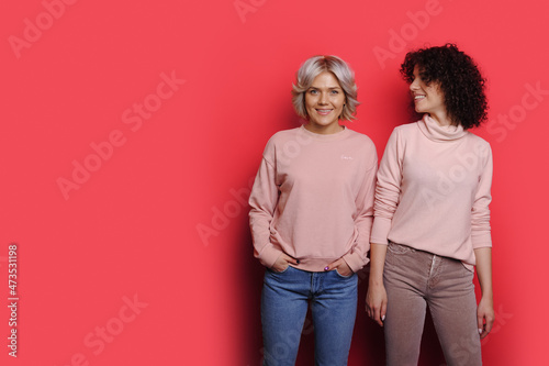 Portrait of two smiling caucasian women standing against pink background with copyspace.