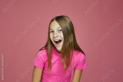 Happy positive exited cute little girl child with open mouth, grimacing, screaming wow on pink studio background