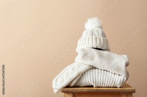 Stylish winter clothes on stool against light background