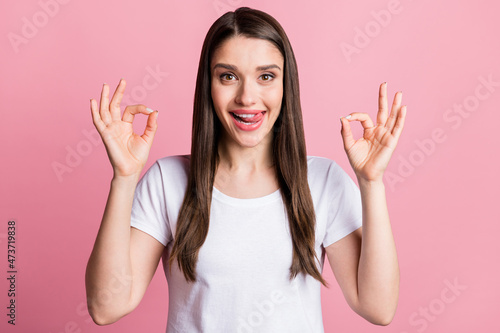 Portrait of attractive cheerful girl showing two ok-sign advert licking lip having fun isolated over pink pastel color background
