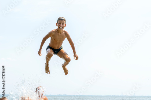 Happy ten years boy jumping in to water on wide river from the air. Summer vacation fun concept