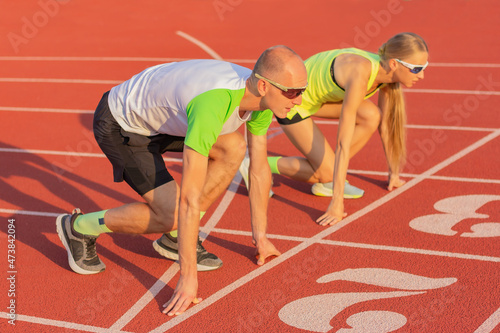 a man and a woman in sportswear on the track of the stadium preparing for a low start of the race, side view. sports, exercise and a healthy lifestyle, competition and gender equality.