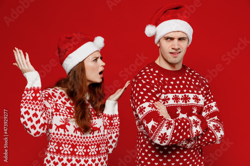 Young angry indignant couple friends two man woman in sweater hat scream shout arguing isolated on plain red background studio portrait. Happy New Year 2022 celebration merry ho x-mas holiday concept.