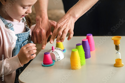 A cute little girl is engaged in a private reception with a woman speech therapist in a playful way with didactic aids