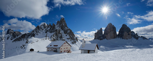 Beautiful panorama of Tre Cime di Lavaredo and Monte Paterno in sunny winter scenery. Locatelli hut and chapel at foot of mountains. Dolomites, Italy