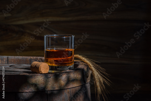 Glass decanter with whiskey, brandy on a vintage background of a rustic oaken barrel. Alcoholic beverage. Still life in the old style