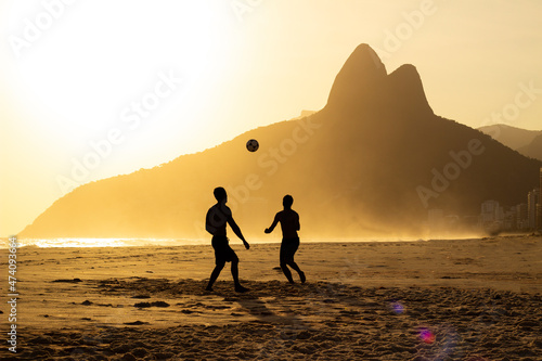 Two Brothers Mountain behind 2 friends playing soccer at Ipanema Beach, Rio de Janeiro. Sunset at summer