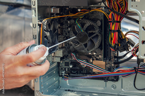 Maintenance and cleaning of the insides of the computer. Man's hand holds a cylinder of compressed air and cleans the insides of the computer