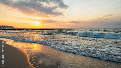 Panorama of the evening sea with a wooden breakwater by the sandy seashore with waves