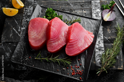 Fresh juicy tuna steak on a black stone plate. On a dark background. Top view.