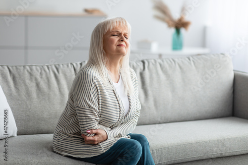 Mature woman suffering from stomachache, touching her tummy