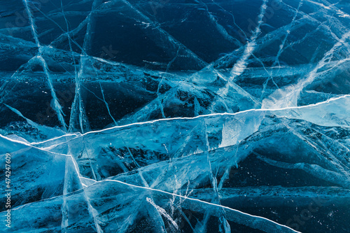 Transparent cracked blue ice on Baikal lake in winter. Abstract winter nature background. Baikal, Siberia, Russia.