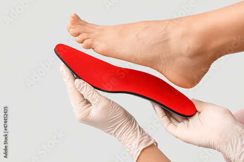 Orthopedist with red insole and female foot on light background, closeup