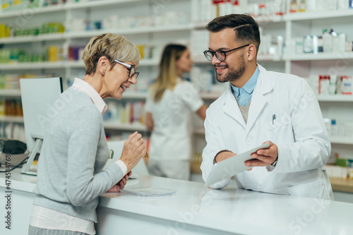 Young male pharmacist giving prescription medications to senior female customer in a pharmacy