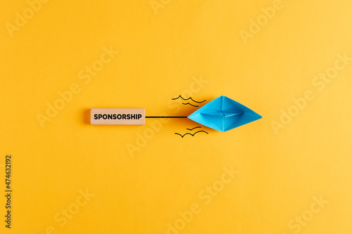 Paper boat pulls a wooden banner with the word sponsorship. Sponsoring, financial support or fundraising