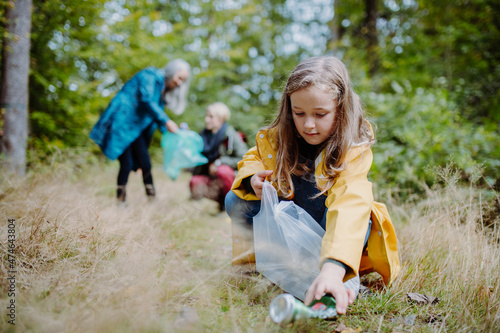 Small girl with mother and grandmother picking up waste outoors in forest.