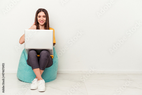Young caucasian woman working with laptop sitting on a puff isolated on white background smiling and raising thumb up