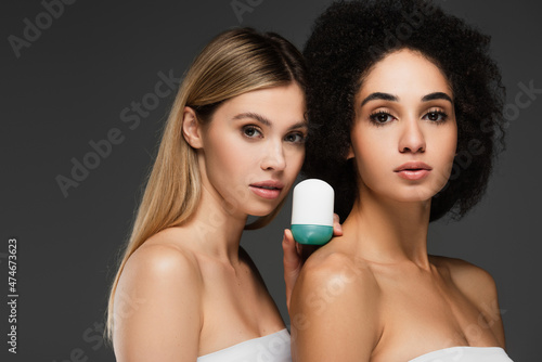 pretty multiethnic women with clean skin and natural makeup looking at camera near deodorant isolated on grey