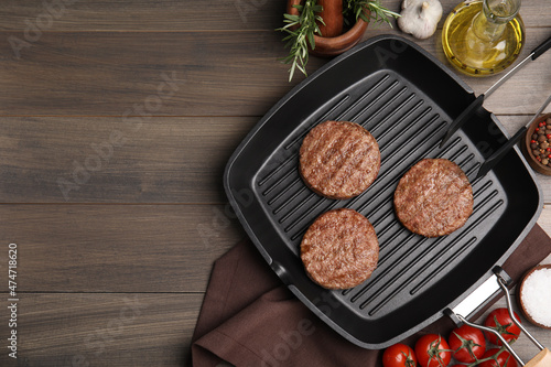 Grill pan with tasty fried hamburger patties and seasonings on wooden table, flat lay. Space for text