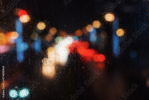Car traffic from behing a wet window after the rain at night background