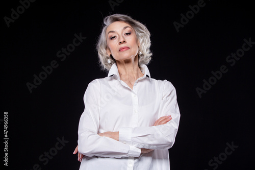 Portrait of a domineering, arrogant mature woman looking down and standing with her arms crossed isolated on a black background