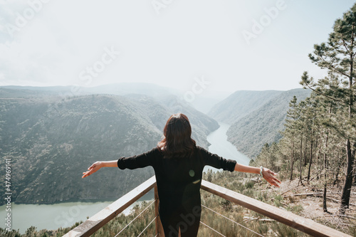 Young beautiful woman traveler looking at beautiful Landscape with a lookout point. Loot of empty sky for your text. Mental health relax and thinking about the future. Freedom, travel, vacation.