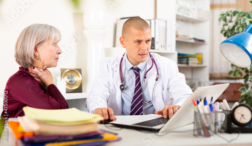 Senior woman visiting qualified doctor in medical office with complaining of sore throat. Focused therapist examining female patient and prescribing treatments while sitting at table