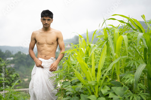 Young Indian fit boy, walking on a pathway beside crops in the field. An Indian priest walking while wearing white dhoti. Indian religious man.