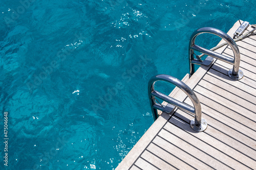 Boat back deck, teak wood and metal ladders, blue sea water background. Luxury yacht cruise